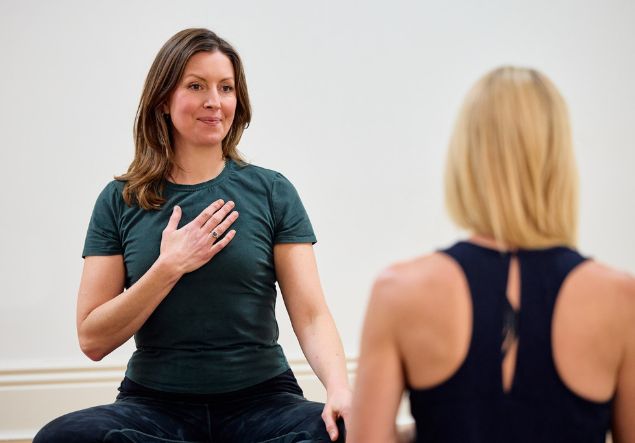 About 4 A woman places her hand on her heart while seated for yoga