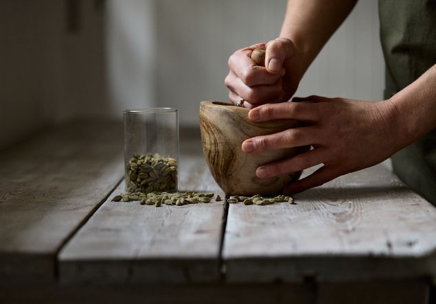 Ayurveda 5 Hands using a wooden pestle and mortar crush up some cardamom pods