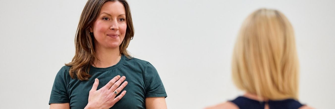 Two women are doing yoga, one with her hand on her heart