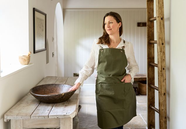 About 1-1 Kate Goodwin, wearing a green apron, places her hand on a large wooden bowl
